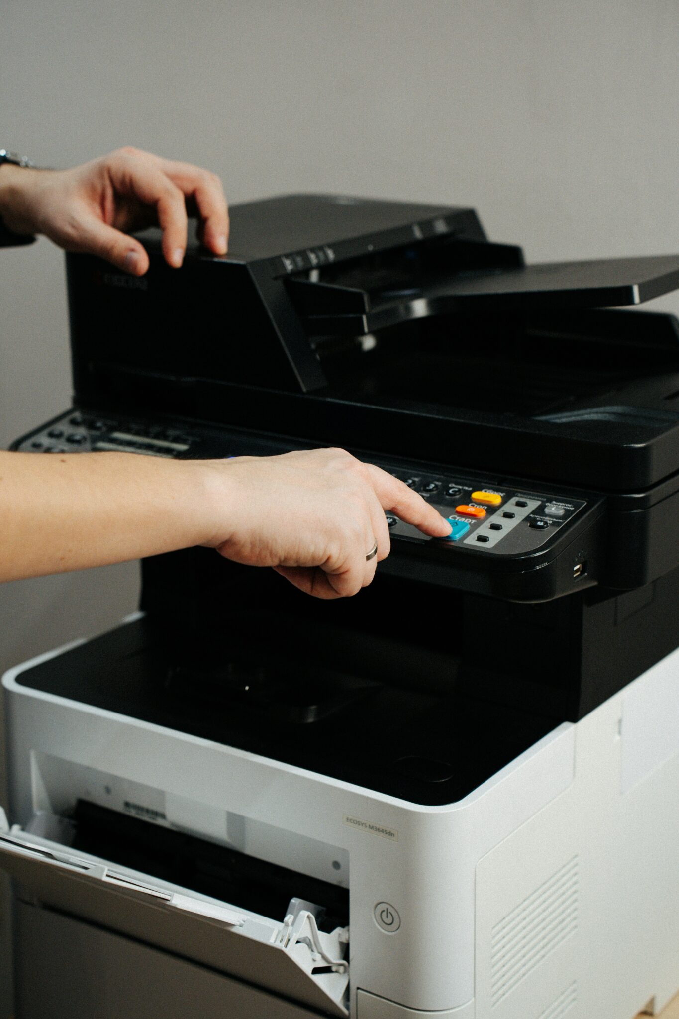 Person bedient einen Multifunktionsdrucker im Büro und drückt die Starttaste, die vordere Geräteklappe ist geöffnet. Symbolbild zur Prüfpflicht für Bürogeräte.